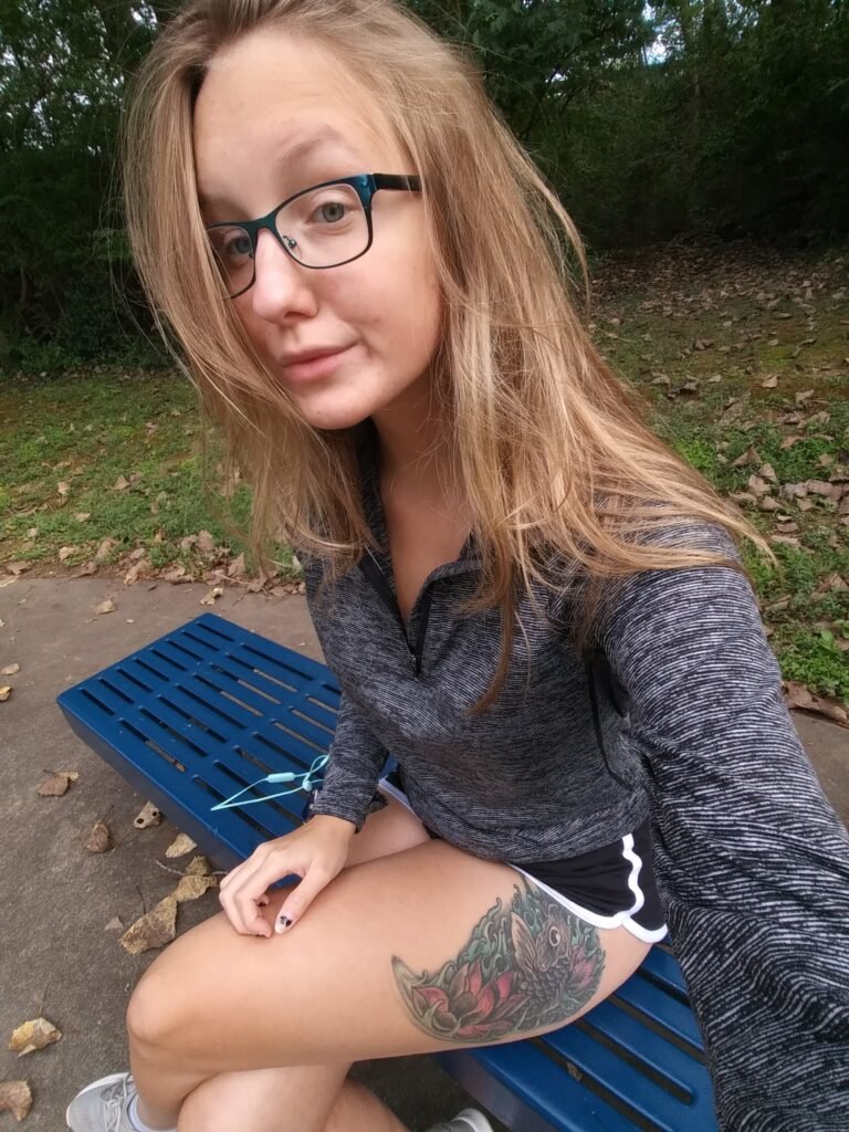 Sitting on a park bench, displaying the koi fish and lotus tattoo, which symbolizes strength, resilience, and personal growth in the face of mental health struggles.